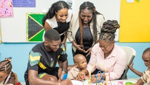 Damion Lowe and a teacher engage with a student at the Early Childhood Centre, as Dominique Walker, CEO of PrintWare Group, and Principal Mrs. Antonica Gunter-Gayle observe.