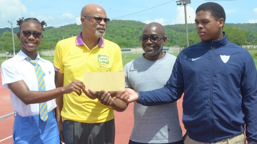   Ray Harvey (second left) co-founder and meet organizer of MILO Western Relays presents a cheque for $210,000 at Jounee Armstrong (L) and Dylan Logan (R) and Coach Abna Stoner of Edwin Allen High School. Harvey called on government to expedite repairs to the running track at the Montego Bay Sports Complex that has been out of commission for the past five years.